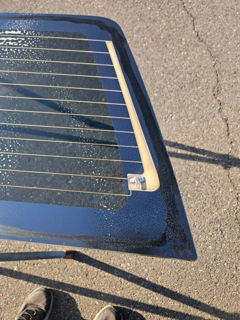Replacement back glass for a 2009 GMC Sierra showing the factory rear defroster electrical connector before installation in Chandler, AZ.