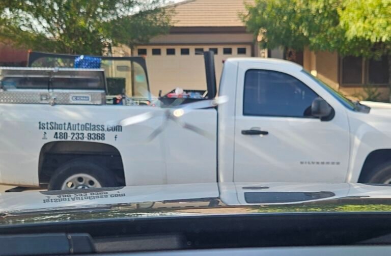 Rock chip in windshield before mobile windshield repair in Gilbert, Arizona, with 1st Shot Auto Glass service truck in the background.