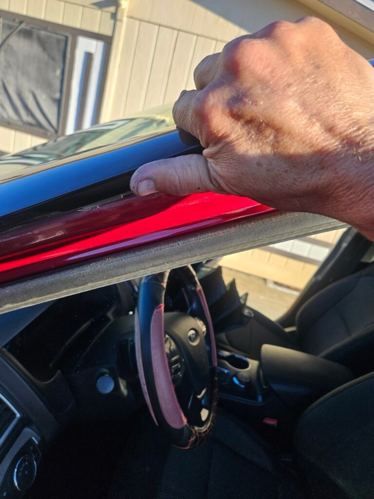 Technician lifting the driver-side windshield molding on a red 2017 Ford Explorer