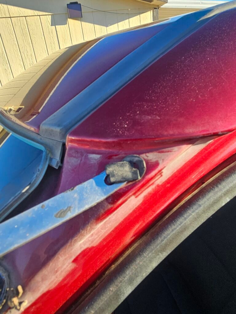 Clip removal tool beneath an old molding clip left in the red Ford Explorer’s upper windshield frame