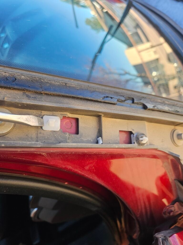Tool positioned against the base of an old windshield molding clip on a red 2017 Ford Explorer