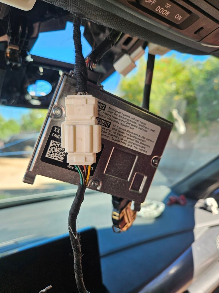 Rearview mirror, rain sensor, and ADAS camera assembly hanging during windshield replacement on a 2024 Acura Integra.